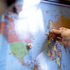 A person adding a thumbtack to a location on a world map.
