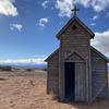 small wooden chapel stands alone in the desert against a blue sky with wispy white clouds