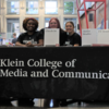 three students sit at a Klein table during a recruitment event and smile
